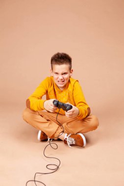 Bir genç duygusal olarak bir bilgisayar ya da konsol oyunu oynar. Çocuk bej bir arka planda oturuyor.