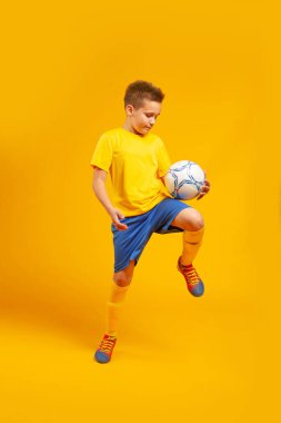 Oğlan sarı arka planda futbol oynuyor.