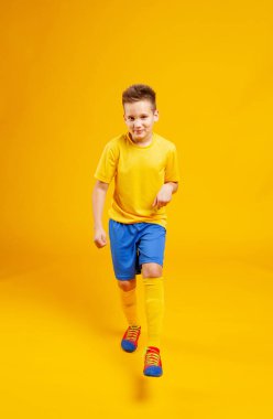 Sarı arka planda futbol forması giyen koşucu çocuk.