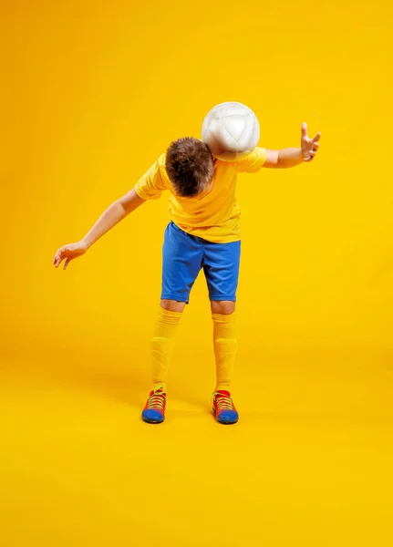 少年は黄色の背景でスタジオでサッカーボールをします — ストック写真