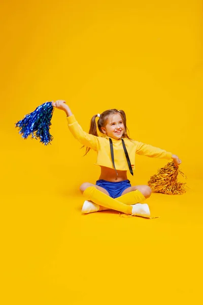 Cute Cheerleader Girl in a Yellow Tank and Blue Shorts Holds Pompons and  Dances / Jumps Stock Image - Image of cheerleading, adorable: 181952739