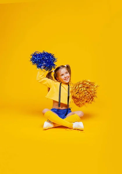 cheerleader girl in a yellow tank and blue shorts holds pompons