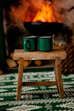 Kulübedeki şöminenin arka planında iki fincan bir taburede duruyor. Kış teması