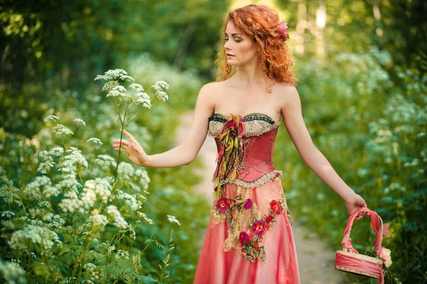 Haired kvinna i en röd klänning samlar blommor. — Stockfoto