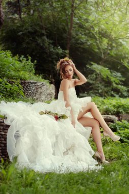 Uzun bacaklı güzel bir gelin ormanda çimlerin üzerinde oturmuş eğleniyor..