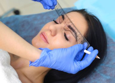 Young beautiful woman making permanent makeup in cosmetology salon. clipart