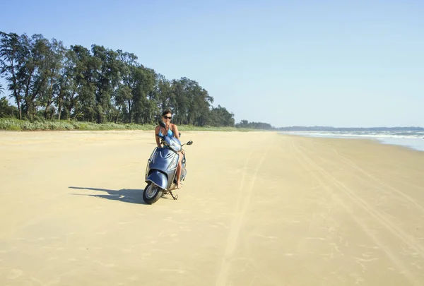 Opalona brunetka jeździ na bezludnej plaży wzdłuż oceanu na mot — Zdjęcie stockowe