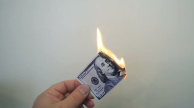 Yanan bir yüz dolarlık banknot tutan el