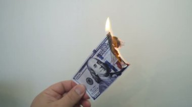 Yanan bir yüz dolarlık banknot tutan el