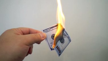 Yanan bir yüz dolarlık banknot tutan el