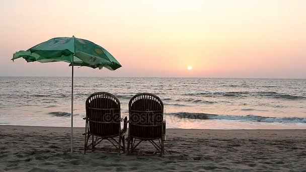 Zwei Liegestühle und Sonnenschirm in Küstennähe bei Sonnenuntergang — Stockvideo