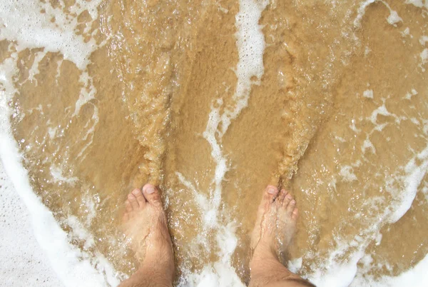 Bovenaanzicht van een man's been permanent op het zand en likte door de o — Stockfoto