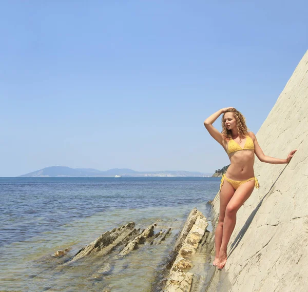 Hermosa rubia posando apoyada sobre roca cerca de la costa del océano — Foto de Stock