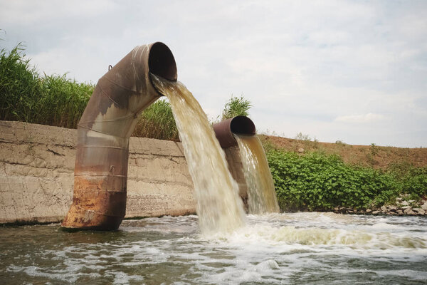 Wastewater from two large rusty pipes merge into the river in cl