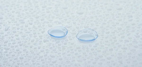 Eye contact lenses on a blue surface covered with drops of water — Stock Photo, Image