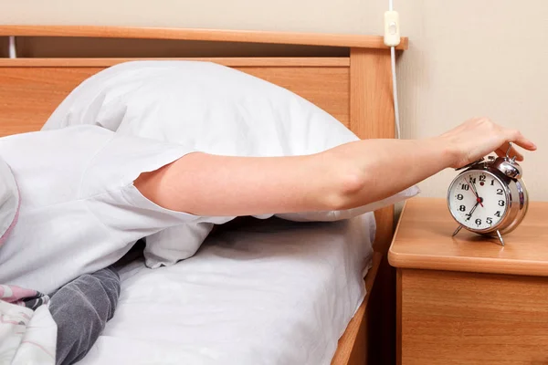 Woman turning off her alarm clock in her bedroom — Stock Photo, Image