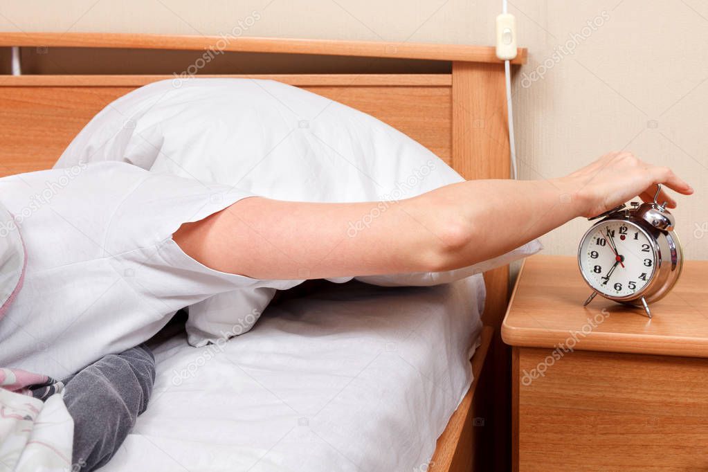 Woman turning off her alarm clock in her bedroom