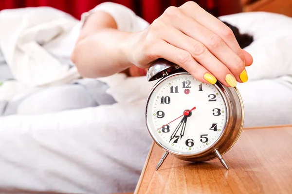 Woman turning off her alarm clock in her bedroom — Stock Photo, Image