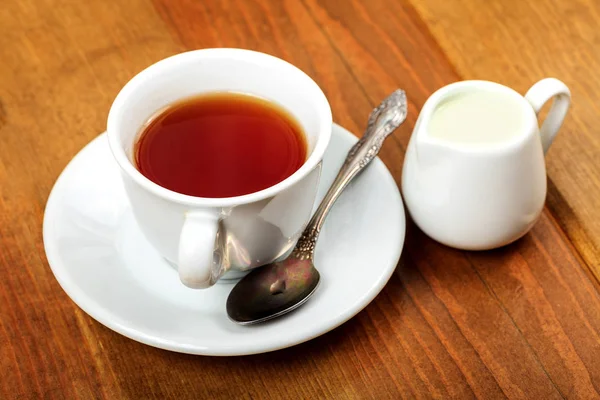 Cup of tea and jug with milk on a wooden table