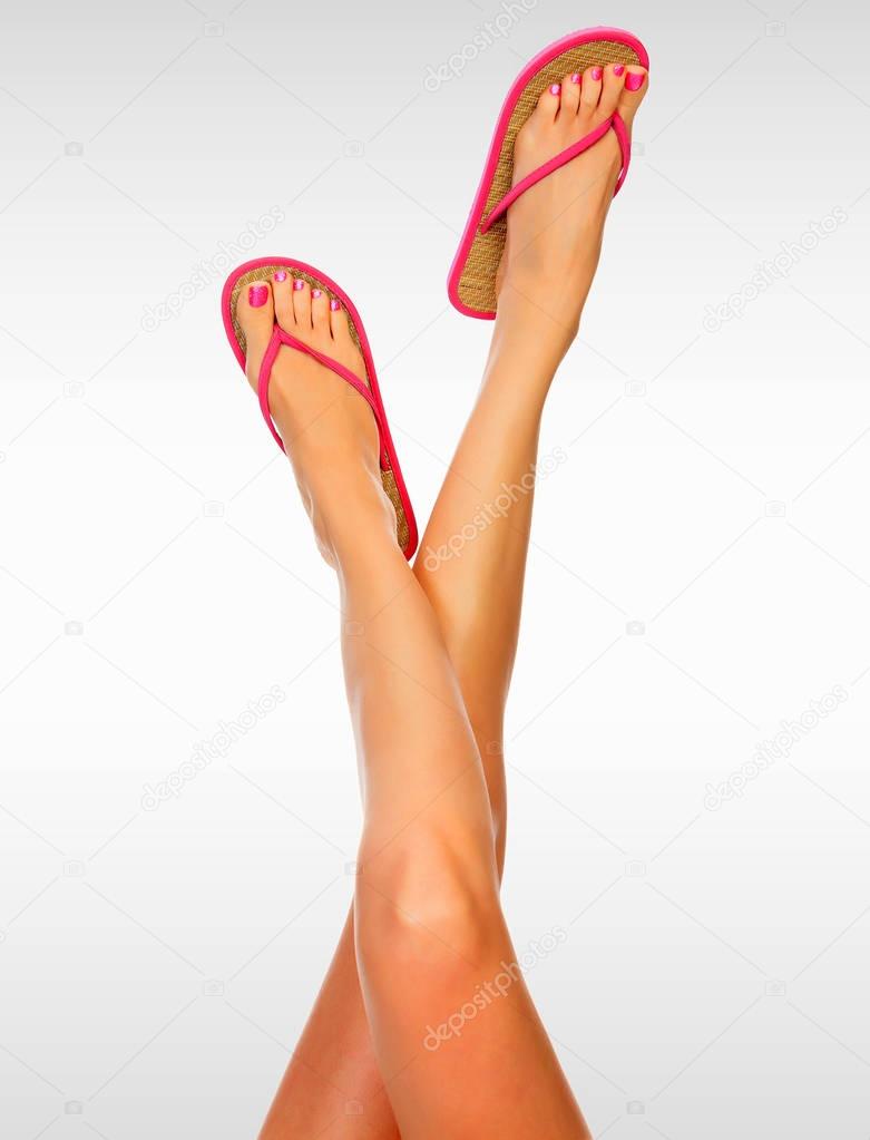 Long woman's legs wearing pink flip-flops against a grey background with copyspace