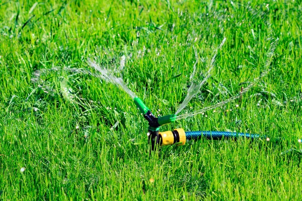 Крупный план газонного разбрызгивателя, поливающего воду над зеленым травяным полем. Система орошения — стоковое фото