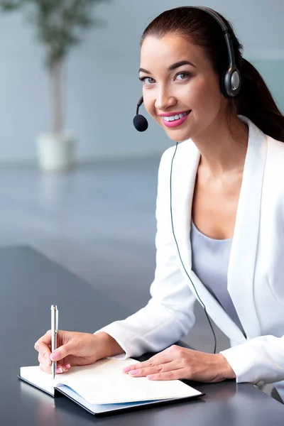 Empresária sorridente ou operadora de helpdesk com fone de ouvido em um escritório — Fotografia de Stock