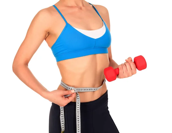 Closeup shot of slim young woman holding red dumbbell and measuring her thin waist with a tape measure, isolated on white background — Stock Photo, Image