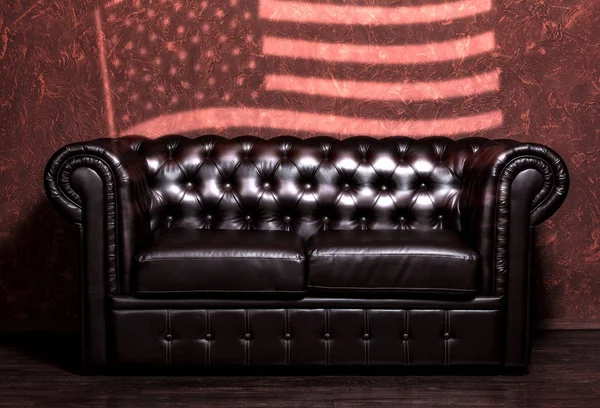 老式的黑色棕色真皮沙发与美国国旗在客厅的垃圾棕色墙 — 图库照片
