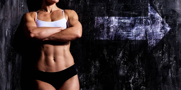 Muskulöse Frau auf dunklem Hintergrund mit weißem Pfeilschild — Stockfoto
