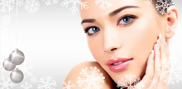 Closeup headshot portrait of a beautiful woman with beauty face and clean smooth soft skin, mild makeup. Grey steel background with snowflakes, christmas baubles and a place for your information — Stock Photo, Image