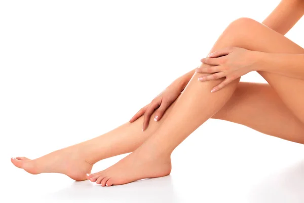 Крупним планом знімок красивих жіночих ніг і рук. Жінка торкається її гладкої шкіри французькими доглянутими руками. Ізольовані на білому тлі — стокове фото