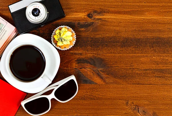 Retro fotocamera, koffiekopje, paspoort, zonnebril en cupcake op bruin houten tafel met ruimte voor tekst, bovenaanzicht. — Stockfoto