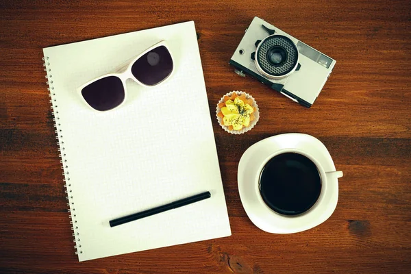 Retro film fotocamera, zonnebril, cupcake, kopje koffie en laptop met potlood op bruin tabel. Bovenaanzicht. — Stockfoto