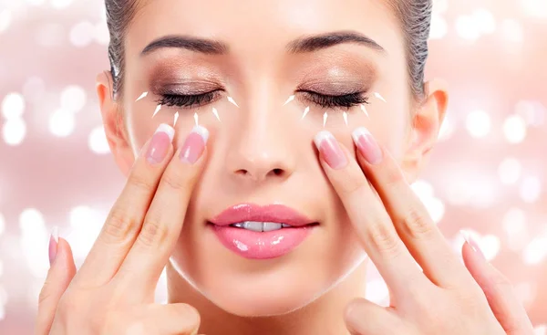 Ładna kobieta masuje jej twarz, koncepcja leczenie skóry. Tło z niewyraźne lights — Zdjęcie stockowe