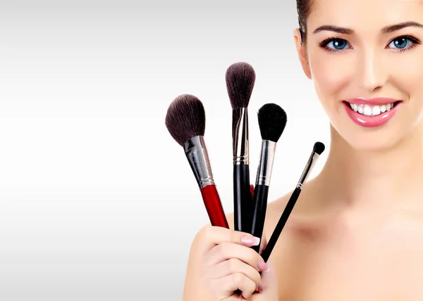 Beauty portrait of lovely beautiful happily smiling woman holding a bunch of make-up brushes against a grey background with copyspace — Stock Photo, Image
