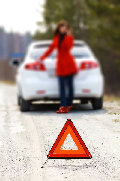 Жінка стоїть біля розбитого автомобіля і попереджувальний знак трикутника — стокове фото