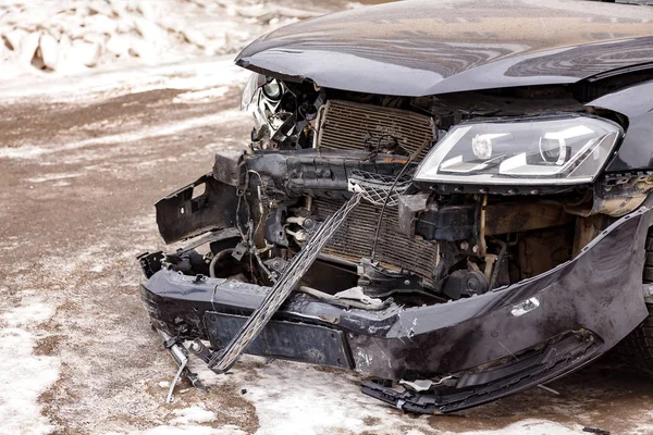 Closeup shot of front part of a black car damaged in accident on the road — Stock Photo, Image