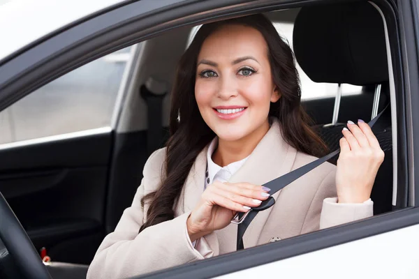 Portrait de jeune femme souriante, heureuse et jolie qui tire sa ceinture de sécurité à l'intérieur d'une voiture blanche . — Photo