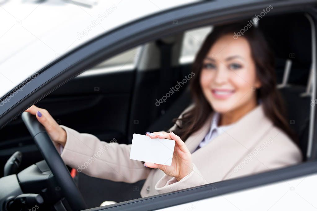 Portrait of smiling woman driver holding a white blank business card. Focus is on the white card