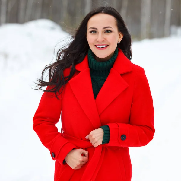 Ganska ung leende kvinna i röd kappa poserar i vinter skog — Stockfoto