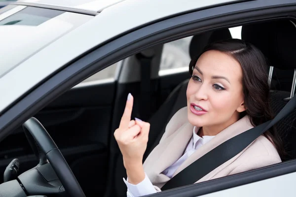 Ładna kobieta kierowca pokazuje środkowy palec do kogoś, boorishness na drogach. — Zdjęcie stockowe
