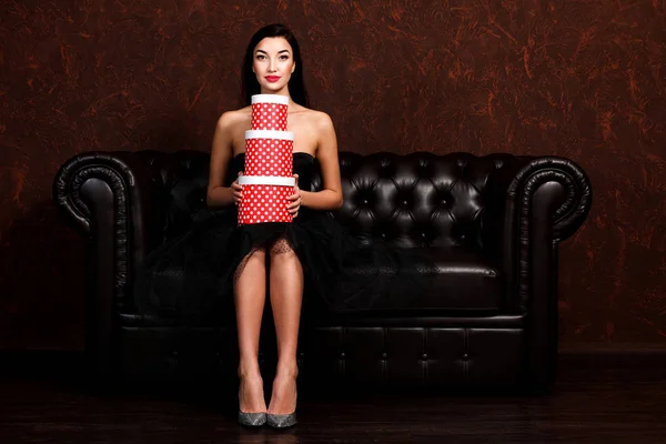 Mulher bonita está sentada no sofá de couro com pilha de presentes — Fotografia de Stock