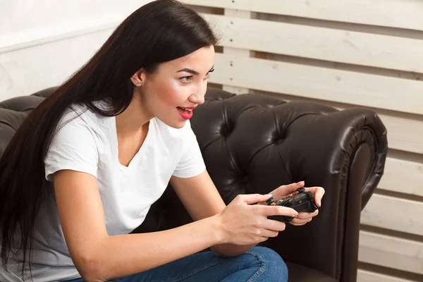 Mujer gamer sentado en el sofá de cuero marrón y jugando un videojuego —  Fotos de Stock