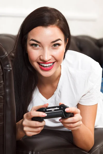 Mujer gamer se encuentra en el sofá de cuero marrón y juega un videojuego — Foto de Stock