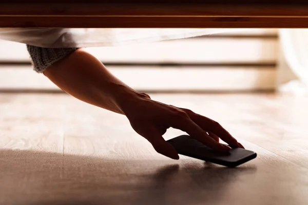 Jemand versteckt ein Smartphone unter dem Bett — Stockfoto