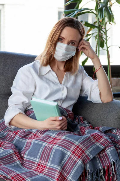 Kvinna Medicinsk Mask Håller Bok Medan Sitter Soffa — Stockfoto