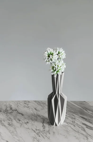 Decorative modern vase with white flowers on gray background.