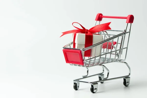 Caja de regalo blanca atada con cinta roja en un carrito de compras —  Fotos de Stock