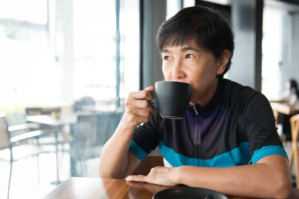 Senior Asian woman with coffee in cycling jersey