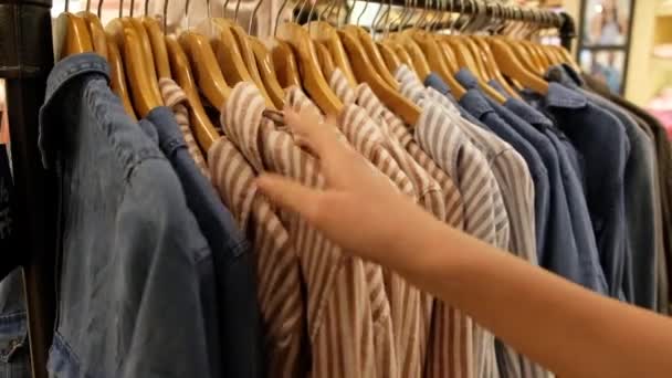 Рука молодой женщины, выбирающей рубашку в универмаге — стоковое видео